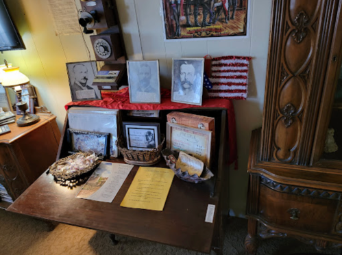 A wooden table displays historical photos, documents, and a small American flag in a cozy room setting.