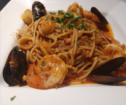 A plate of spaghetti topped with shrimp, mussels, and herbs in a rich tomato sauce.