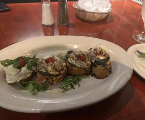 A plate of bruschetta topped with cheese, cherry tomatoes, and arugula, served on a white dish with a wooden table background.