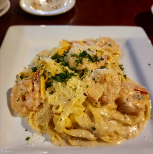 A plate of creamy fettuccine pasta topped with shrimp, parsley, and grated cheese.