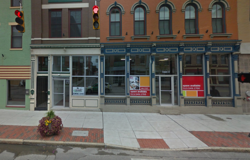 Street view of a commercial building with vacant storefronts and a traffic light, featuring "space available" signs.