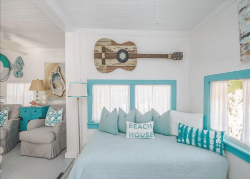 Cozy beach house interior with a guitar on the wall, light blue accents, and a comfortable daybed with decorative pillows.