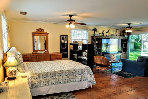 Cozy bedroom with a queen bed, wooden furniture, bookshelves, and large windows overlooking a garden.