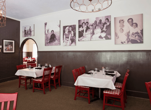 Cozy restaurant interior with red chairs, white tables, and black-and-white family photos on the wall.