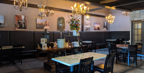 Cozy restaurant interior with wooden tables, black chairs, chandeliers, and decorative wall art.
