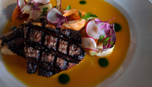 Grilled fish fillet on a vibrant orange sauce, garnished with radishes, herbs, and colorful vegetables.