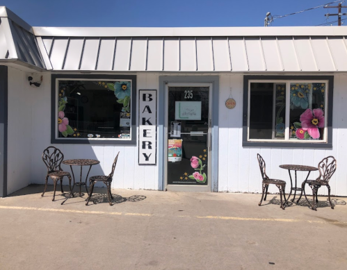 A charming bakery storefront with floral decorations, featuring a door and two outdoor tables with chairs.