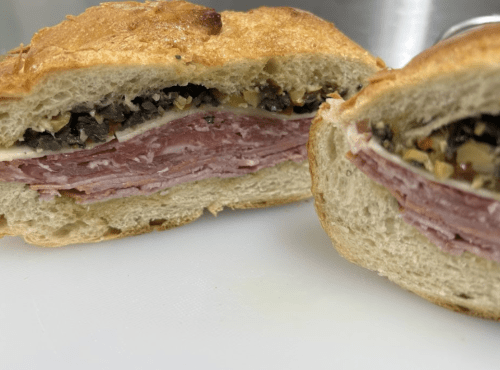Close-up of a sliced sandwich with layers of meats and a spread, served on crusty bread.
