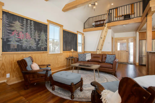 Cozy living room with wooden accents, chalkboard art, and comfortable seating, featuring a staircase to a loft area.