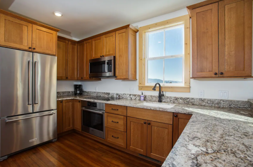 Modern kitchen with wooden cabinets, stainless steel appliances, and a granite countertop, featuring a window with a view.