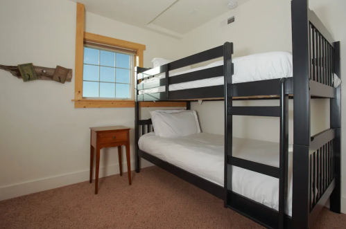 A cozy room featuring a black bunk bed and a small wooden nightstand beside a window.