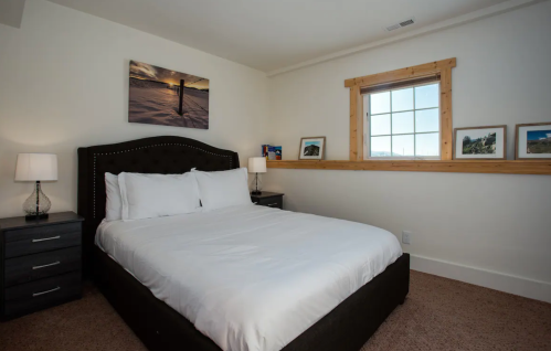 Cozy bedroom with a queen bed, nightstands, lamps, and a window featuring scenic artwork on the wall.