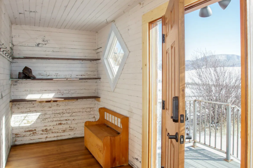 A rustic entryway with a wooden bench, shelves, and a diamond-shaped window, leading to a snowy outdoor view.