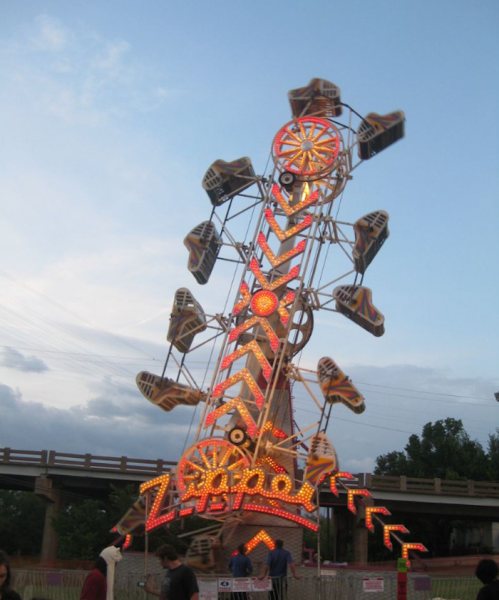 A brightly lit Ferris wheel with colorful seats against a cloudy sky, with people gathered below.
