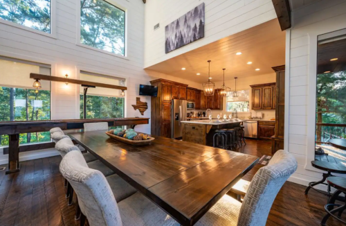 A spacious dining area with a wooden table, stylish chairs, and a modern kitchen in a bright, airy room.