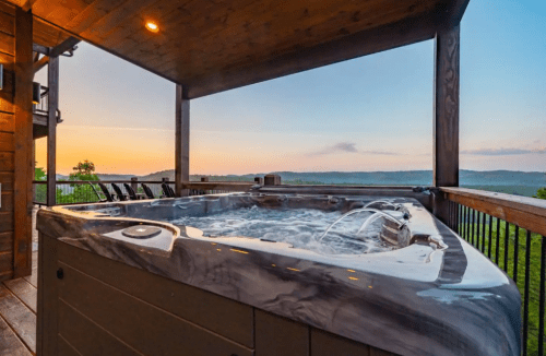A hot tub on a wooden deck with a scenic view of hills and a colorful sunset in the background.