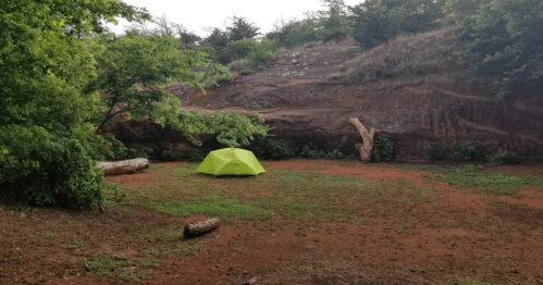 A bright green tent set up in a grassy area surrounded by trees and a rocky hillside.