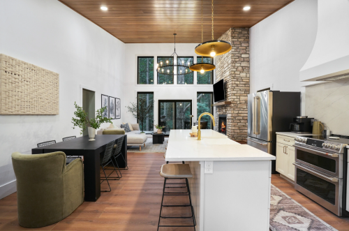 Modern kitchen and dining area with a large island, stone accents, and large windows overlooking greenery.