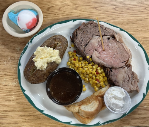 A plate with sliced roast beef, baked potato with toppings, corn, toast, and a small dessert of ice cream.