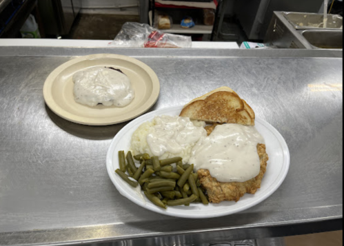 A plate of fried chicken with gravy, green beans, mashed potatoes, and toast, alongside a dessert on a separate plate.