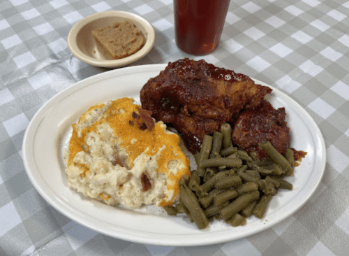 A plate of fried chicken with barbecue sauce, green beans, cheesy mashed potatoes, and a slice of cornbread.