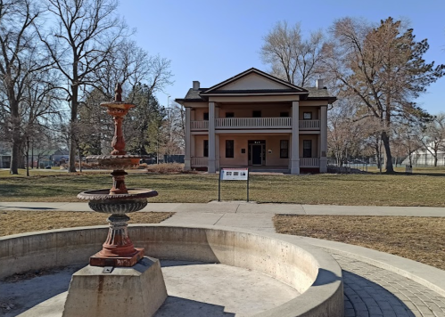 A historic building with a fountain in the foreground, surrounded by trees and a clear blue sky.