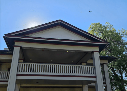 A close-up of a building's upper facade with a balcony, under a clear blue sky and sunlight.