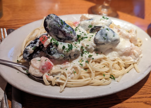 A plate of linguine topped with creamy sauce, mussels, and diced tomatoes, garnished with parsley.
