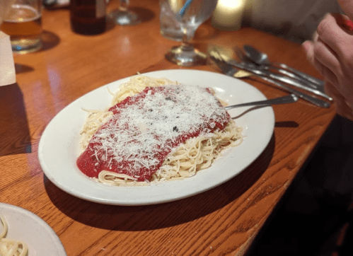 A plate of spaghetti topped with marinara sauce and grated cheese, set on a wooden table with utensils nearby.