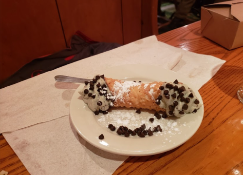 A plate with a cannoli filled with cream and topped with chocolate chips and powdered sugar.