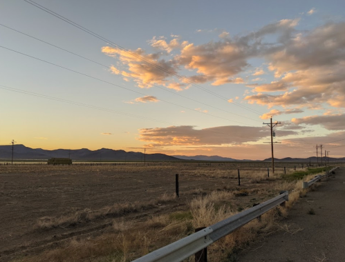 A serene landscape at sunset, featuring mountains, clouds, and power lines along a rural road.