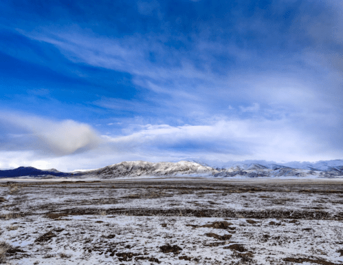A vast snowy landscape with mountains in the distance under a blue sky with scattered clouds.