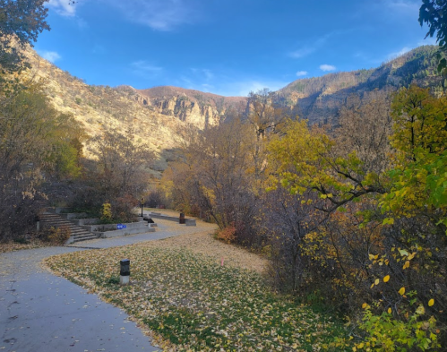 A scenic pathway through a colorful autumn landscape, surrounded by mountains and trees with yellow leaves.