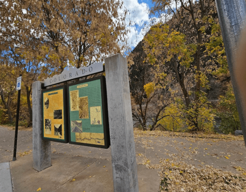 Information sign about Colorado, surrounded by autumn foliage and a scenic landscape.