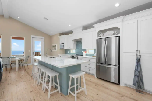 Bright, modern kitchen with white cabinets, stainless steel appliances, and a large island with seating. Natural light flows in.