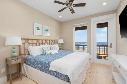 Cozy bedroom with a blue and white bedspread, lamps, and ocean view through large windows.