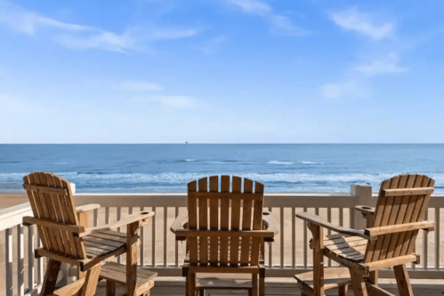 Two wooden chairs on a deck overlooking a calm ocean under a clear blue sky.