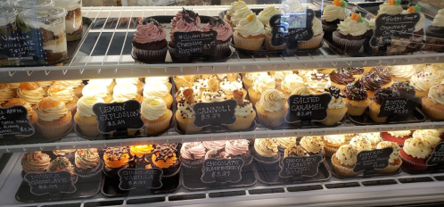 A display case filled with various colorful cupcakes, each labeled with flavors and prices.