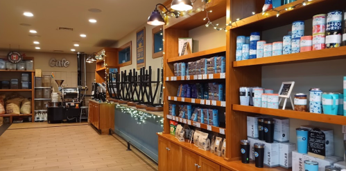 A cozy café interior with shelves of tea and coffee products, wooden counters, and festive lights.