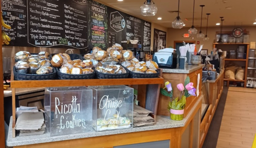 A cozy bakery counter with baskets of cookies, a menu board, and a vase of tulips.