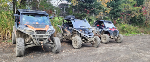Three off-road vehicles parked on a dirt path, surrounded by greenery and autumn foliage.