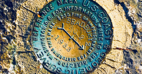 A bronze survey marker embedded in a stone surface, labeled "U.S. Coast & Geodetic Survey" with a date of 1938.