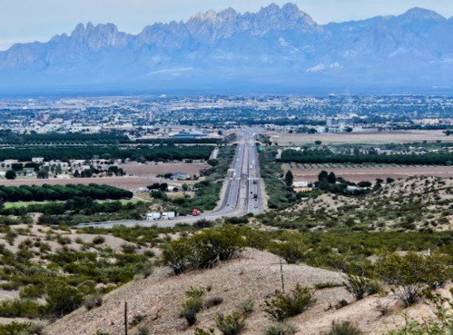 A wide highway stretches through a valley, with mountains in the background and fields on either side.