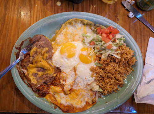 A plate of food featuring two eggs, refried beans with cheese, rice, and a side of lettuce and tomato.