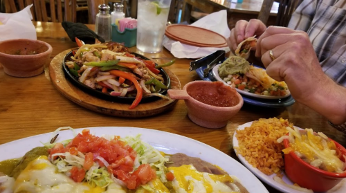 A table with a variety of Mexican dishes, including fajitas, tacos, rice, and beans, in a cozy restaurant setting.