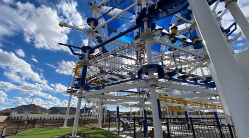 A large industrial structure with blue and white components under a partly cloudy sky, surrounded by mountains.