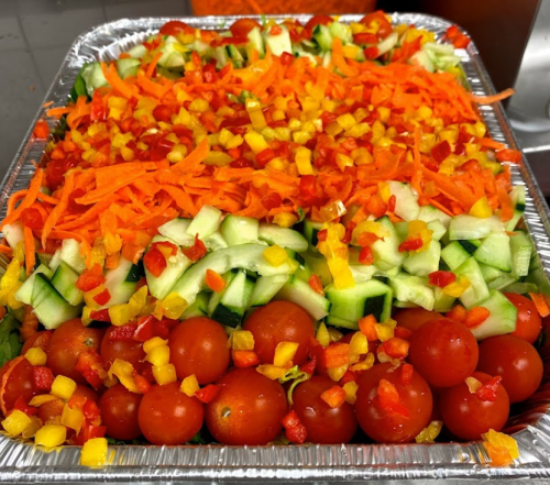 A colorful tray of fresh vegetables, including shredded carrots, diced cucumbers, and cherry tomatoes.