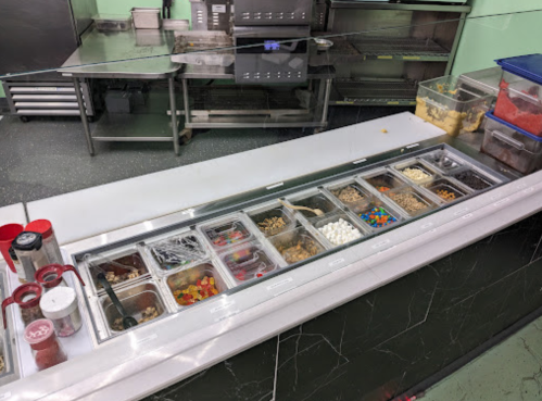 A countertop with various toppings in clear containers, including candies and sprinkles, in a kitchen setting.