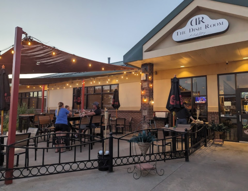 Outdoor dining area of The Dish Room, featuring string lights, tables, and patrons enjoying their meals.