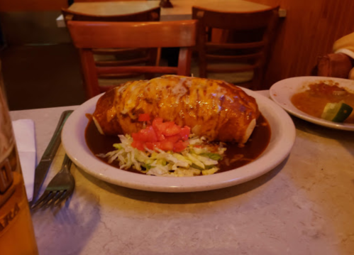 A large enchilada topped with cheese, served on a plate with lettuce and diced tomatoes.